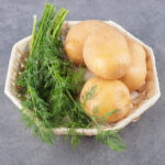 A white plate of uncooked potatoes with fresh dill . High quality photo